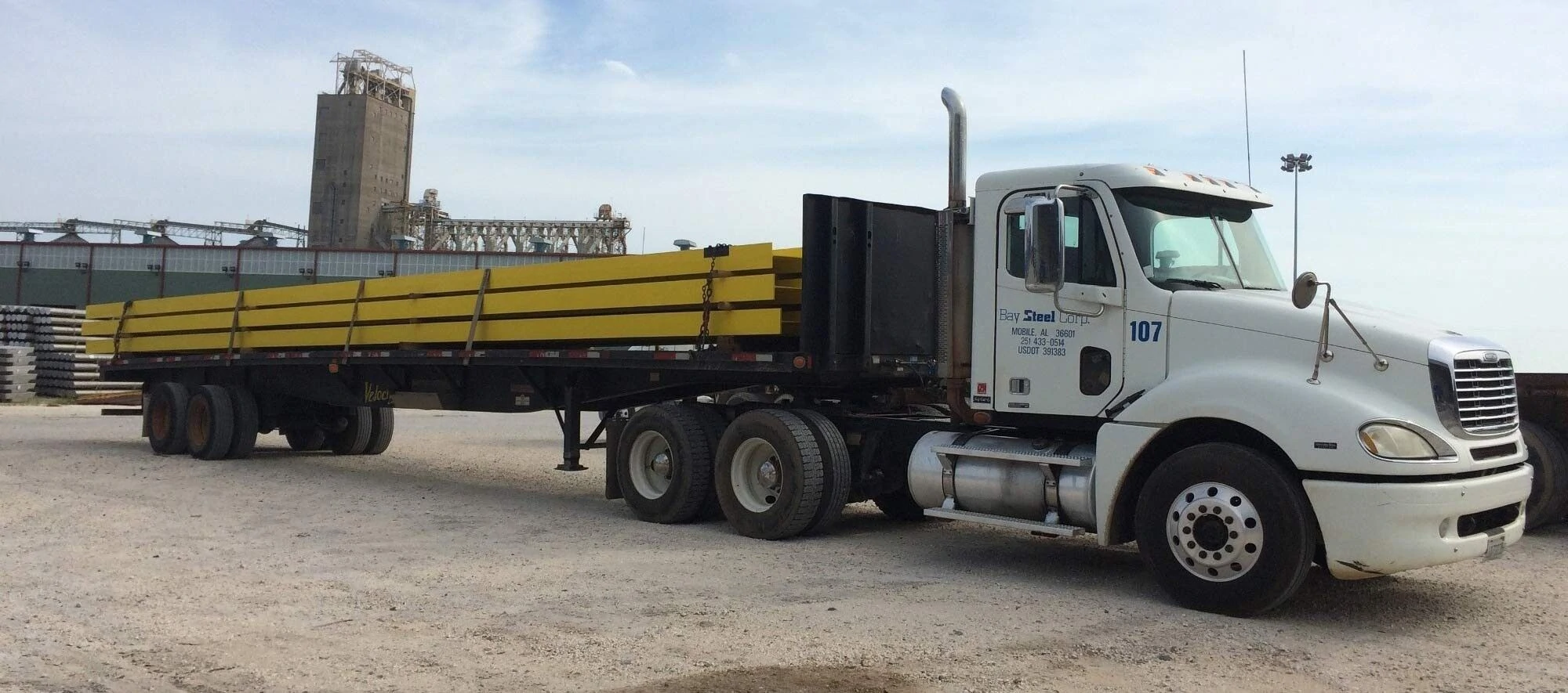 A flatbed truck with yellow cargo parked in an industrial area